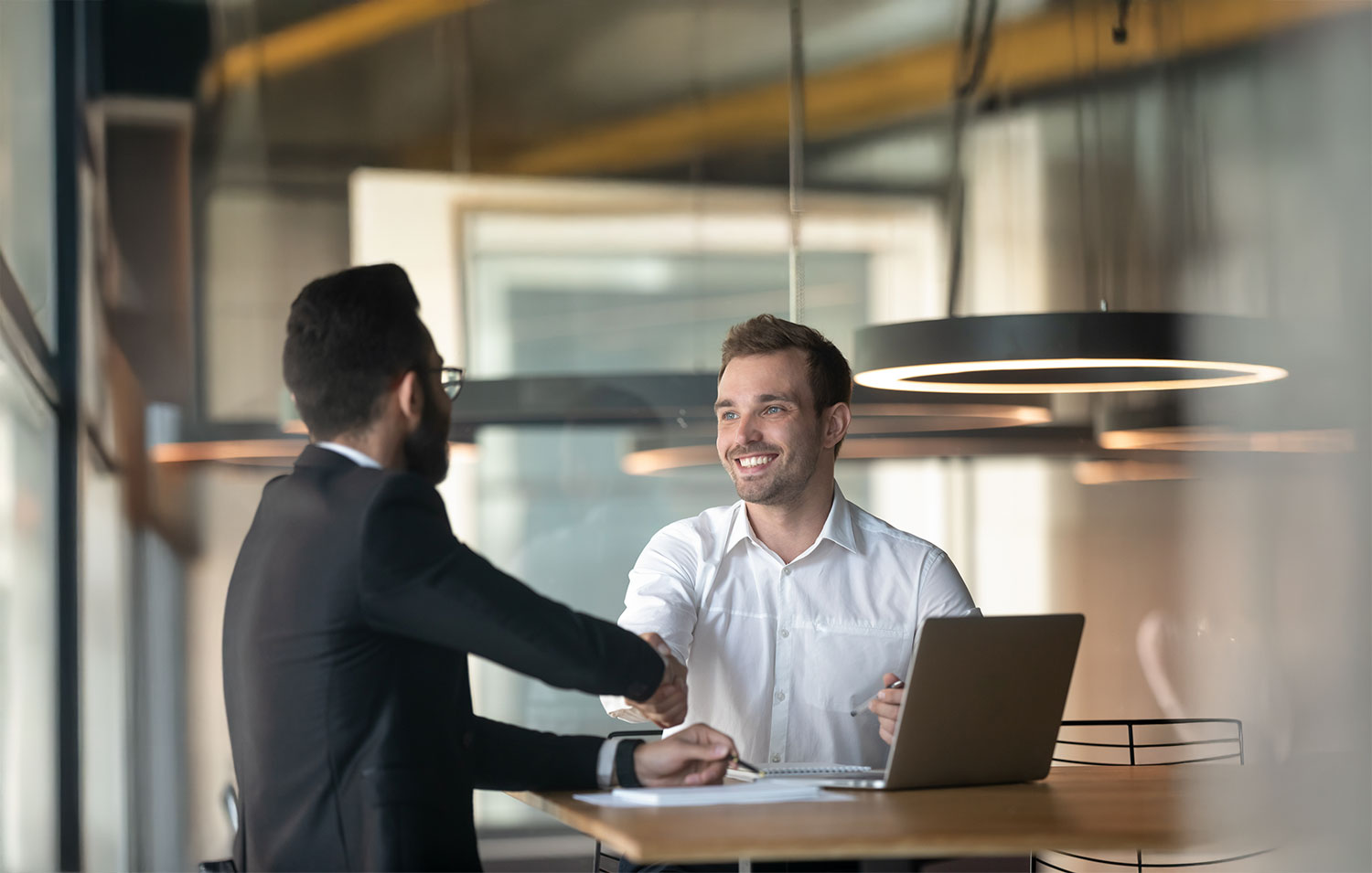 Business professionals shaking hands over an office lease agreement in a modern workspace.